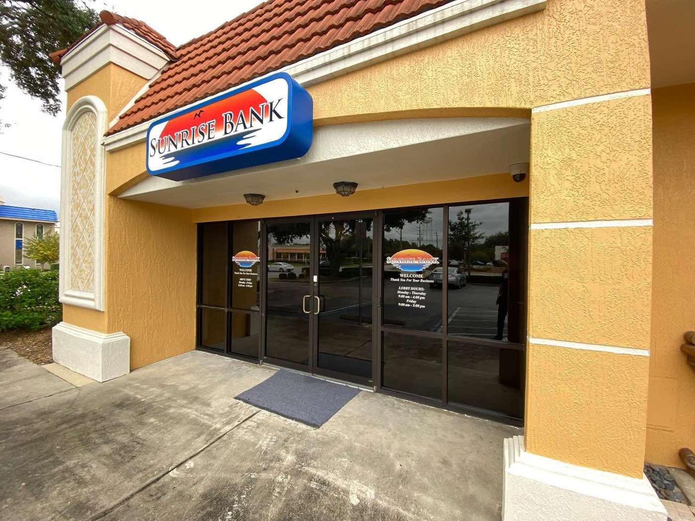 Outside view of the Sunrise Bank storefront with tinted glass doors — dark and private from the exterior