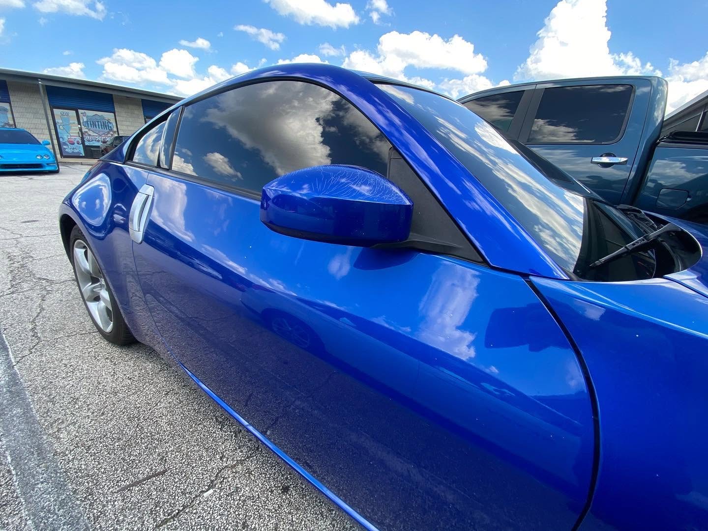 Blue sports coupe with dark ceramic window tint outside Mitchell's Tinting shop